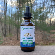 Bottle of Elderflower Botanicals Daily Defense immune support liquid extract on a wooden surface with a forest background.