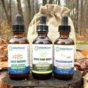 Three bottles of elderflower botanicals on a wooden stump with a forest background