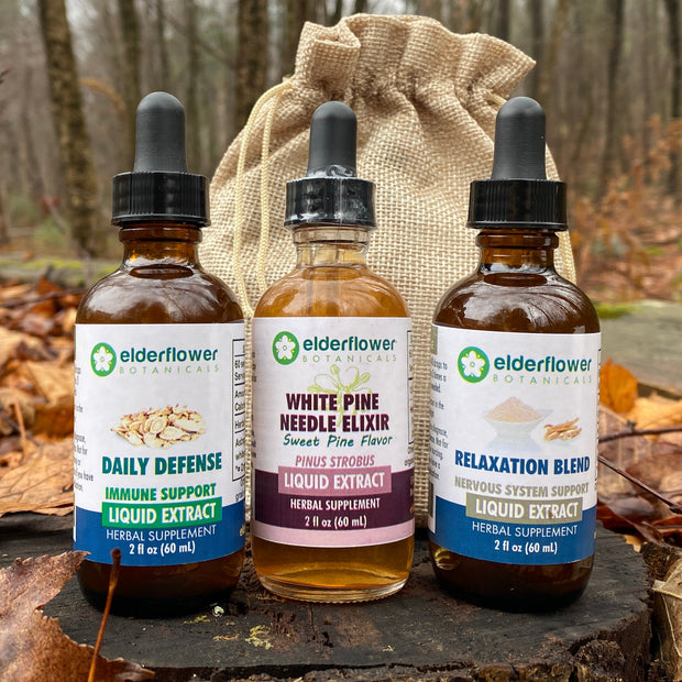 Three bottles of elderflower liquid extract on a wooden stump with a burlap bag in a forest setting.