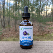 Bottle of Elderflower Botanicals Restful Sleep with Melatonin Liquid Extract on a wooden surface with a forest background.