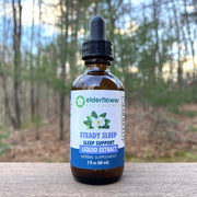 Bottle of Elderflower Botanicals Steady Sleep Liquid Extract on a wooden surface with a forest background